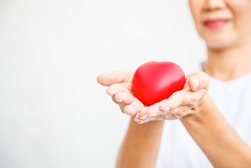 Selective Focus Of Red Heart Held By Smiling Female Nurse's Both