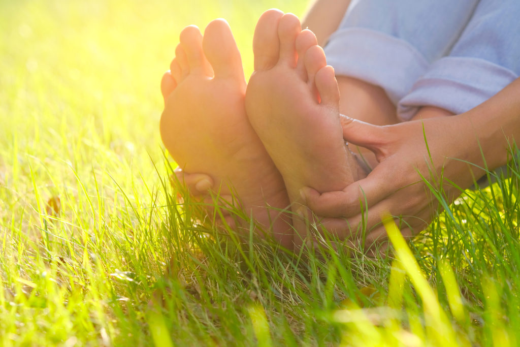 Foot Pain .woman Sitting On Grass Her Hand Caught At The Foot. H